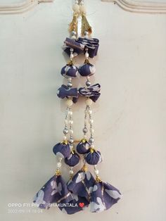 a purple and white necklace hanging from a hook on a wall with pearls attached to it