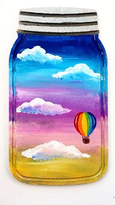 a painted mason jar with a hot air balloon in the sky and clouds on it