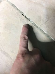 a person's hand on the floor pointing at something with their thumb and index finger