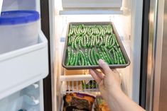 a person is holding an open refrigerator door with green beans in it and the food inside