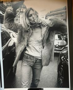 a black and white photo of a woman in a fur coat walking down the street