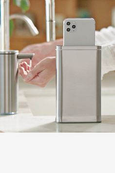 a person holding a cell phone in front of a trash can on a counter top