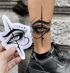 a person with a tattoo on their leg holding up a sticker that has an eye