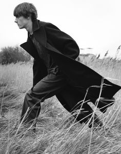 black and white photograph of man in long coat walking through tall grass