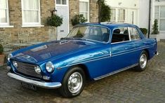 an old blue car parked in front of a brick building on a cobblestone street