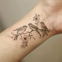 two birds sitting on a branch with flowers tattooed on the arm and wrist tattoo design