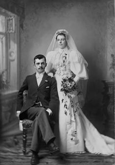 an old black and white photo of a man and woman dressed in wedding attire, sitting next to each other