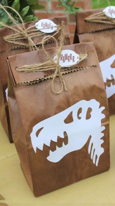 three brown paper bags with dinosaur designs on them sitting on a table in front of some plants