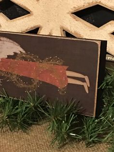 a sign with an angel on it sitting next to some pine branches and snowflakes