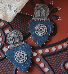 two blue and white earrings on top of a red tablecloth with beads around the edges