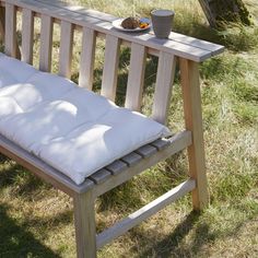 a wooden bench sitting in the grass next to a bowl of fruit on top of it