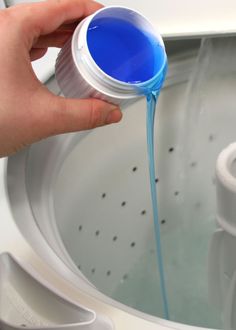 a person is pouring blue liquid into a washing machine