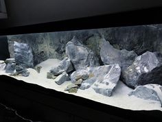 an aquarium filled with rocks and water in the middle of a dark room next to a wall