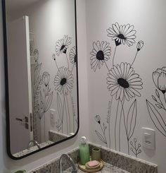 a bathroom sink under a large mirror with flowers painted on the wall next to it