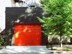 a red garage door in front of a black building with trees and bushes around it