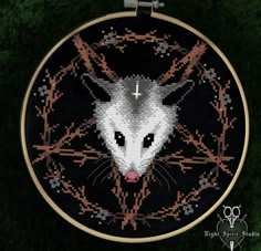 a cross - stitch picture of a white rat with black eyes in a circular frame