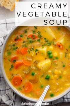 a bowl of soup with carrots, peas and bread on a towel next to it