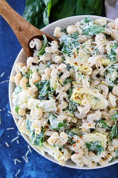 a pasta salad with spinach and cheese in a white bowl on a blue surface