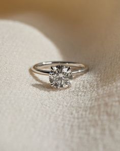 a diamond ring sitting on top of a white cloth next to a light colored background