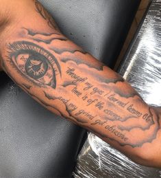 a man's arm with an all seeing eye tattoo on it and some clouds in the background