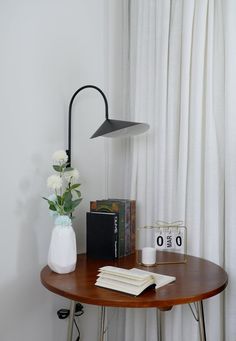 a wooden table topped with a white vase filled with flowers next to a black and white clock