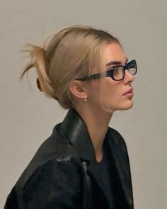 a woman wearing glasses and a black jacket with her hair in a high pony tail