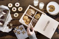 a person holding a cookie box with cookies in it and other treats on the table