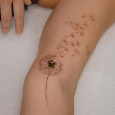 a woman's arm with a dandelion tattoo on the back of her leg