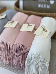 three pink and white blankets sitting on top of a table next to a basket with tags