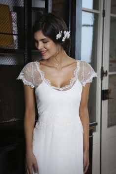 a woman in a white dress standing next to a door and smiling at the camera