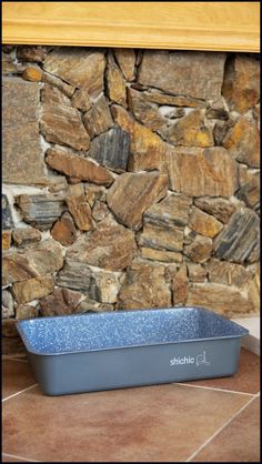 a blue rectangular dish sitting on top of a tile floor next to a stone wall