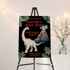 a dinosaur birthday party sign on an easel in front of a string of lights