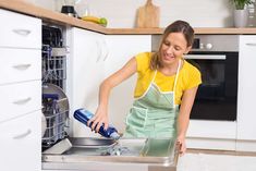 a woman in an apron is washing dishes with a sprayer and a blue bottle