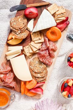 an assortment of cheeses, meats and fruit on a cutting board