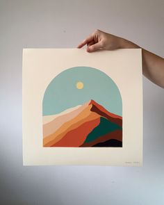 a person holding up a paper with an image of a mountain in the background and a full moon above it