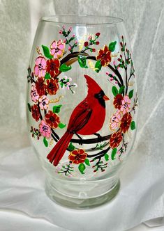 a glass with a red cardinal painted on it's side sitting on a white surface