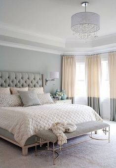 a bedroom with a large bed, chandelier and two windows in the background