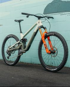 an orange and white mountain bike parked in front of a blue wall with graffiti on it