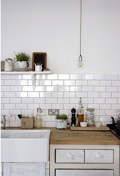 a kitchen with white tiles and wooden counter tops, pots on the shelf above the sink