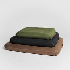 three pillows stacked on top of each other, one black and one green with an orange flower