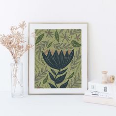 there is a vase with some flowers in it next to a framed print on the wall