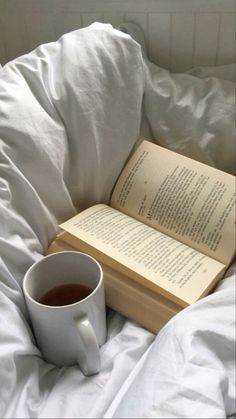 a cup of tea and an open book on a bed with white comforter,