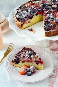 a piece of cake on a plate with berries and powdered sugar next to it