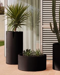 three black planters sitting next to each other on a brick floor near a window