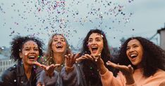 three women are laughing and throwing confetti in the air