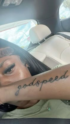 a woman is sitting in the back seat of a car and has her arm tattooed with words that read, god's speed