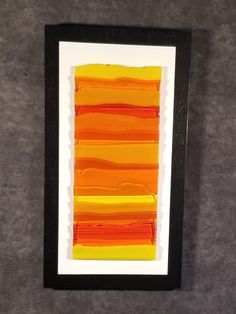 an orange and yellow piece of art hanging on a wall next to a black frame