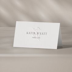 a white business card sitting on top of a bed next to a beige sheet with the name kate wyatt written on it