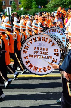 a marching band with orange and white uniforms is on the street in front of a large crowd