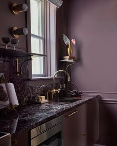 a purple kitchen with marble counter tops and gold faucets on the windowsill